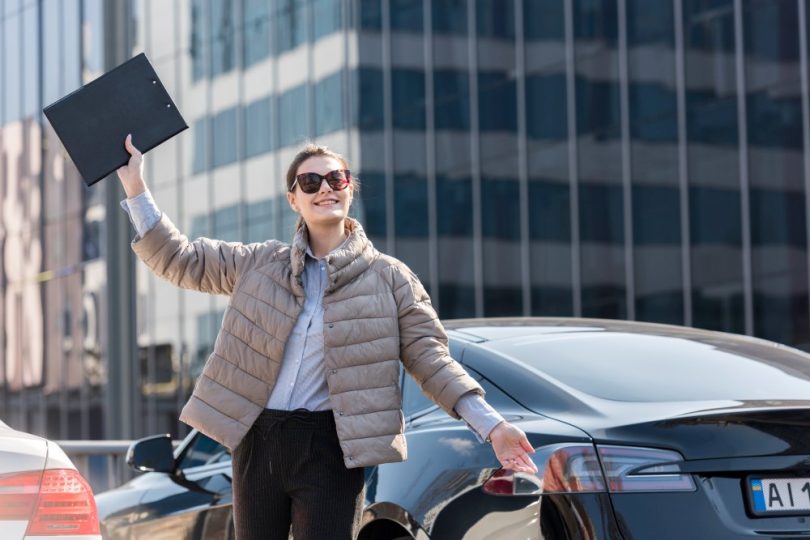 devojka pored automobila sa podignutom fasciklom u ruci