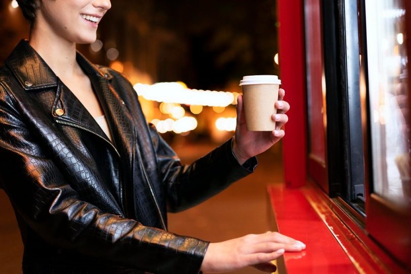 zena sa kafom u ruci ispred automata