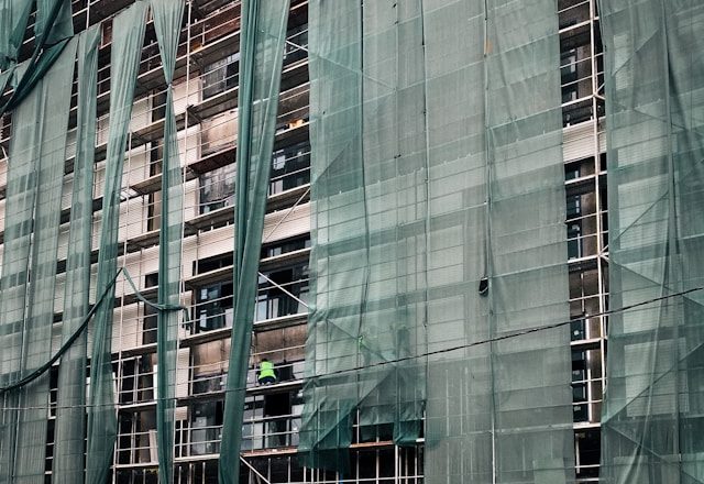 Zgrada pod skelom prekrivenom zelenom mrežom i radnik u fluorescentnom prsluku