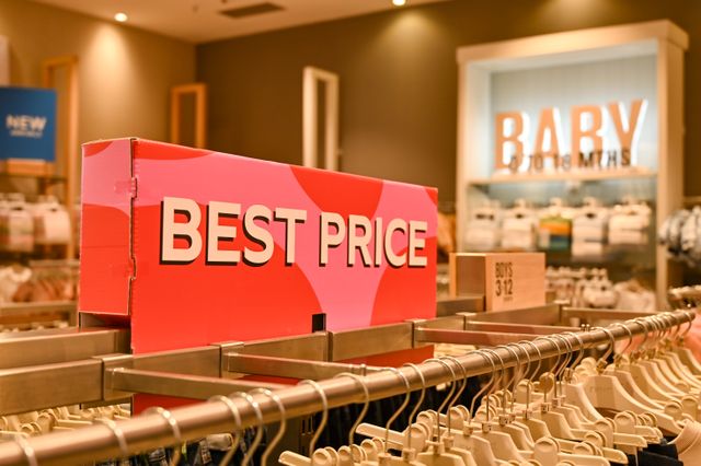 Ružičasti znak sa natpisom BEST PRICE iznad police sa vešalicama u prodavnici