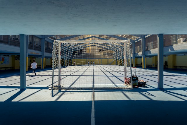 Gol sa mrežom na natkrivenom sportskom terenu sa senkama i decom u pozadini